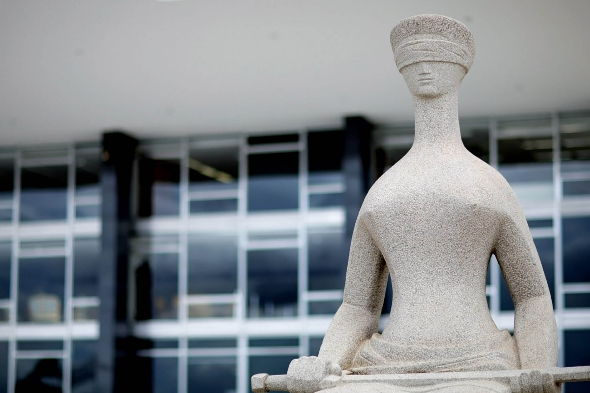 Direito penal: Estátua moderna da Justiça, simbolizando a imparcialidade com seus olhos vendados, o equilíbrio com a balança e a força da lei com a espada, em frente a um prédio institucional.